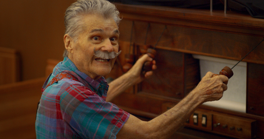 Still of Fred Willard in a 2020 “I Think You Should Leave” sketch where by mistake he is hired to play a whimsical fotoplayer at a funeral